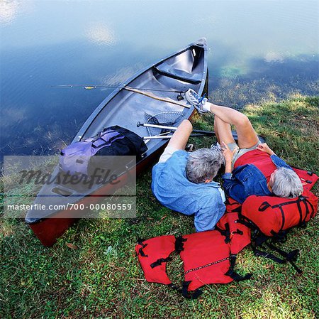 Back View of Mature Couple Relaxing on Shore with Canoe