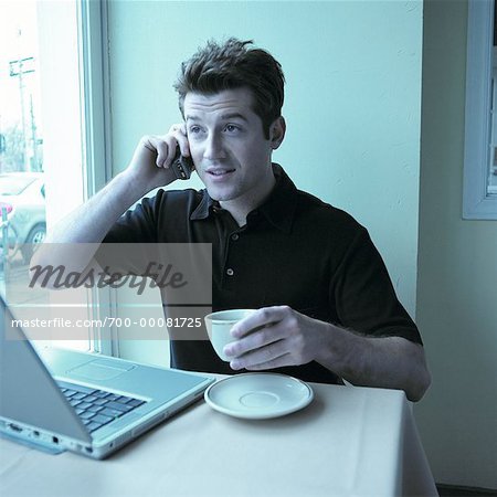Mann mit Handy im Cafe mit Laptop am Tisch