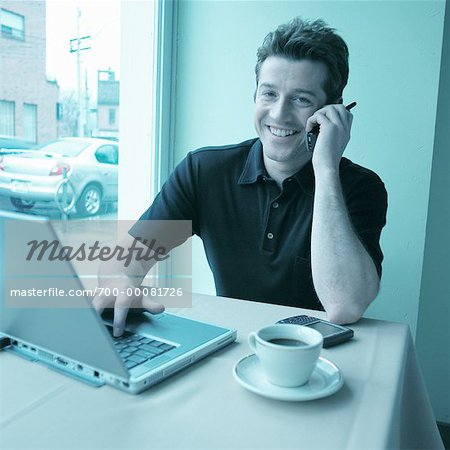Portrait of Man Using Cell Phone In Cafe with Laptop Computer on Table