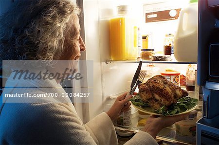Mature femme debout au réfrigérateur ayant poulet comme collation de minuit