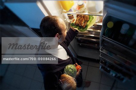 Homme debout au réfrigérateur, prise de poulet, pain et légumes