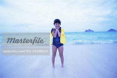 Portrait de jeune fille en maillot de bain debout sur la plage, tenant des palmes