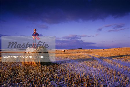 Child in Superhero Costume Standing on Haystack in Field With Snow