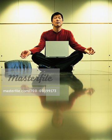 Man Meditating on Boardroom Table With Laptop