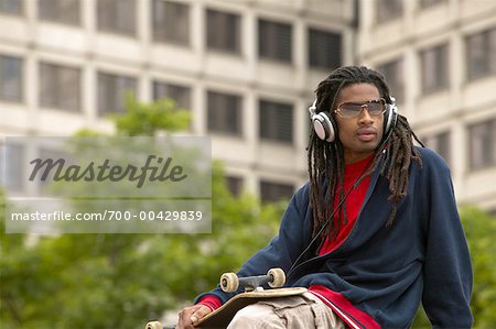 Man Listening to Headphones and Holding Skateboard