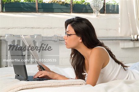 Femme allongée sur le lit avec ordinateur portable et le journal