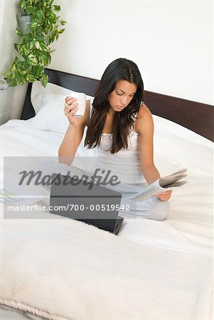 Frau sitzt auf dem Bett mit Zeitung und Laptop