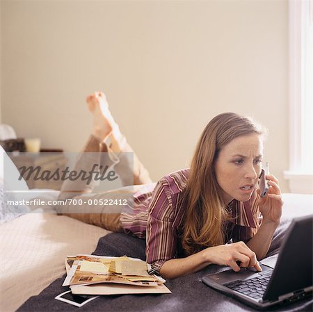 Femme au lit avec un téléphone cellulaire et ordinateur portable