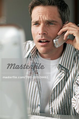 Man Looking at Computer Screen and Using Cellular Telephone