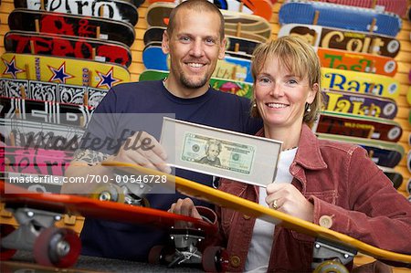 Couple Holding Framed Dollar Bill in Skateboard Store