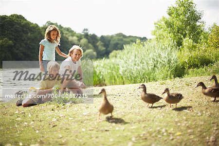 Grandmother and Grandchildren Feeding Ducks