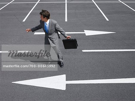 Businessman in Parking Lot, Standing Between Arrows