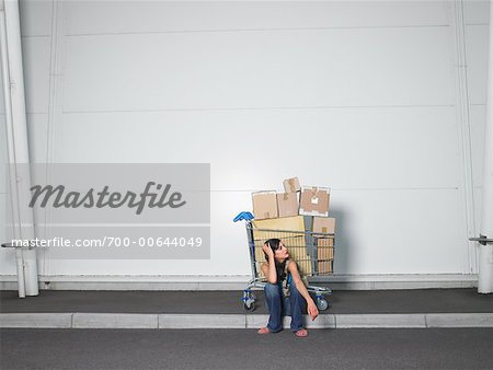Woman Sitting on Curb With Grocery Cart Full of Boxes