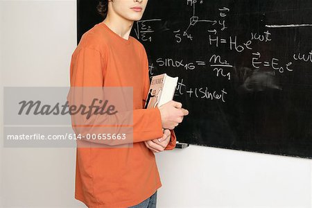 Young man with book in front of blackboard