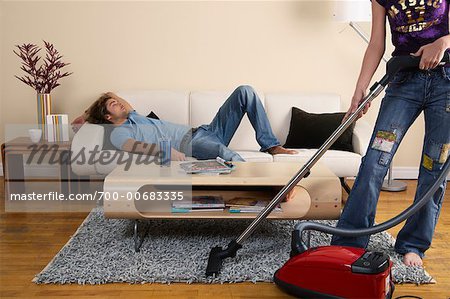 Woman Vacuuming while Man Sleeps on Sofa