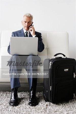 Businessman Using Cellular Phone and Laptop on Business Trip