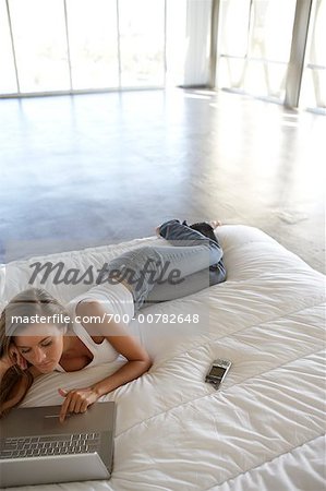 Frau auf dem Bett liegend, mit Laptop