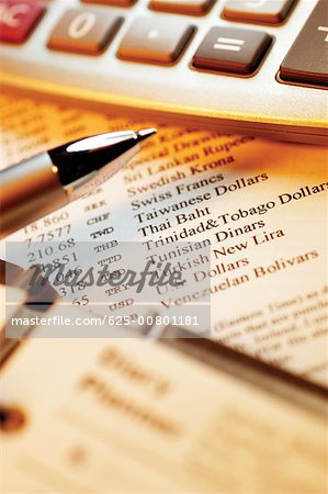 Calculator and pen on top of currency exchange rate information, close-up