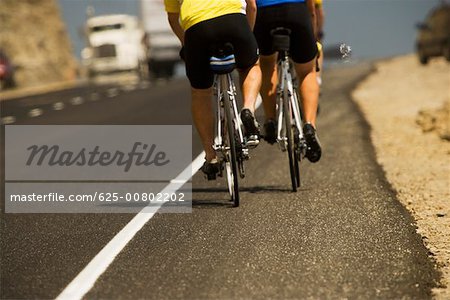 Low section view of two people riding cycles on a road
