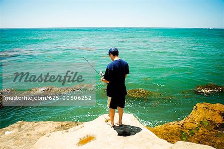 Rückansicht eines Mannes Angeln von einem Felsen, Pazifischer Ozean, Coronado Riffe, San Diego, Kalifornien, USA