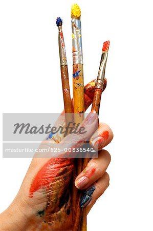 Close-up of a person's hand holding paintbrushes