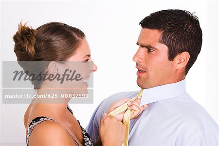 Side profile of a young woman pulling a mid adult man with his tie