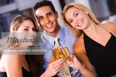 Two young women and a young man toasting with champagne flutes