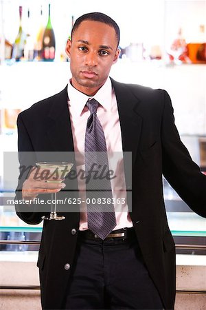 Portrait d'un homme d'affaires appuyé contre un bar comptoir tenant un verre de martini