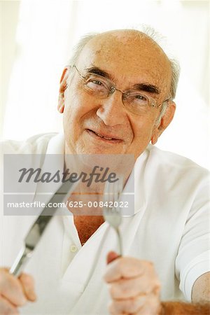 Portrait d'un homme senior tenant une fourchette et un couteau de table