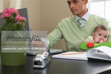 Businessman Using Laptop Computer, Holding Baby