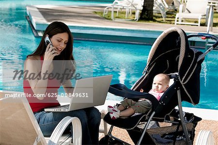Mère parler sur un téléphone mobile avec sa fille à côté d'elle au bord de la piscine