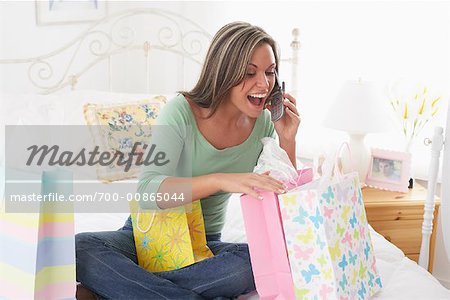 Femme au lit avec les sacs à provisions et téléphone cellulaire