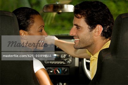 Young woman and a mid adult man sitting in a car looking at each other