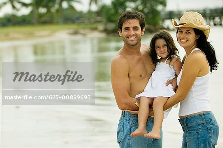 Portrait of parents carrying their daughter on the beach