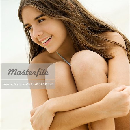 Gros plan d'une adolescente, assis sur la plage souriant
