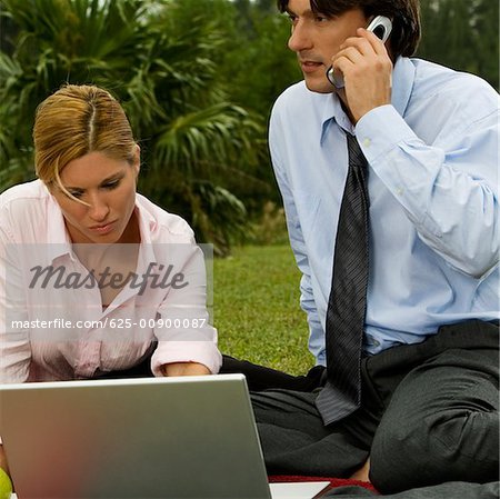 Gros plan d'un homme d'affaires parlant sur un téléphone mobile avec une femme d'affaires à l'aide d'un ordinateur portable