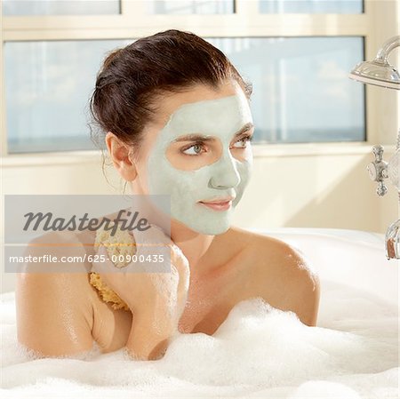 Gros plan d'une jeune femme avec un masque facial tenant une éponge de bain