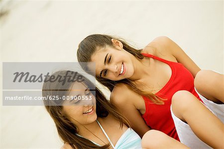 Vue grand angle sur une fille et une jeune adolescente, assis sur la plage souriant