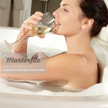 Profil de côté d'une jeune femme tenant un verre de vin dans une baignoire