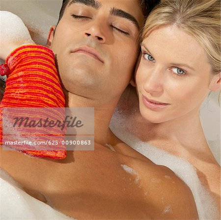 Close-up of a young woman scrubbing a young man's chest with a bath sponge