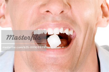 Gros plan d'un jeune homme tenant un morceau de sucre entre ses dents