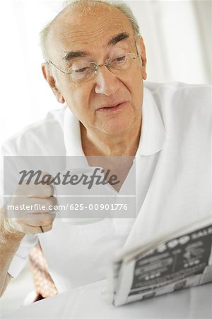 Close-up of a senior man holding a cup of coffee reading a newspaper