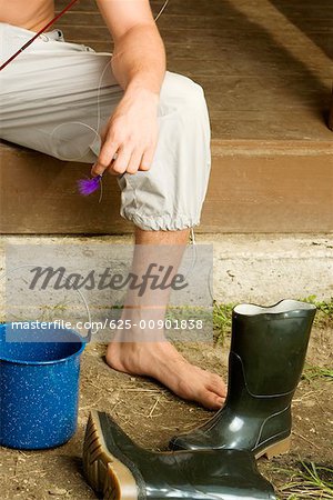 Low section view of a young man sitting on the porch with a bucket and a pair of boots