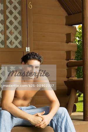 Portrait of a bare chested young man sitting on the porch and smiling