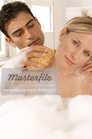 Close-up of a young man scrubbing a young woman's neck with a bath sponge