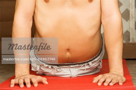 Mid section view of a bare chested young man performing the cobra pose