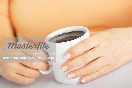 Mid section view of a senior woman holding a cup of black coffee