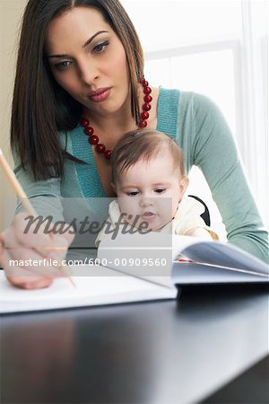 Mère écrit dans le cahier, avec bébé sur ses genoux