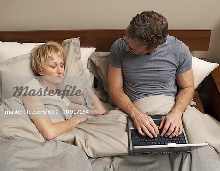 Couple avec ordinateur portable dans le lit