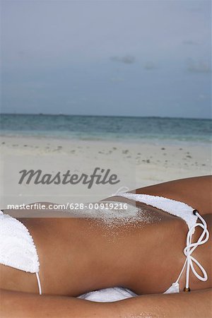 Young girl wearing bikini lying on the beach, sand on belly